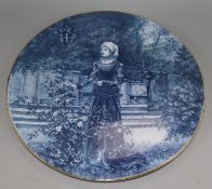 A blue-glazed circular ceramic wall plaque depicting a medieval lady in a garden, Dia 16in approx