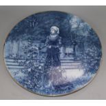 A blue-glazed circular ceramic wall plaque depicting a medieval lady in a garden, Dia 16in approx