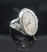 An 18ct white gold ring watch, with oval open face Arabic dial and carved foliate shoulders and