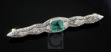 A gold and platinum, emerald and diamond set bar brooch, the central emerald measuring 7.1mm by 7.