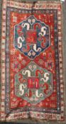 A Kazak red ground rug, c.1885, with two central polygons in a field of stylised figures and motifs,