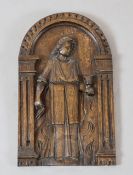 A 17th century arched oak panel, carved with a standing robed figure, 13 x 8in.