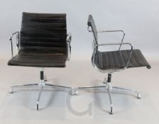 A pair of Charles and Ray Eames revolving desk chairs, with ribbed black leather seats, Vitra labels