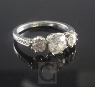 A platinum and three stone diamond ring, with diamond set shoulders, the central round cut stone