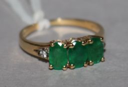 A 14ct gold three stone emerald ring, with diamond set shoulders, size L.