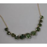 An Edwardian 9ct gold and green garnet? necklace, set with eleven round and oval cut stones, 44cm.