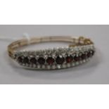 A Victorian style yellow metal, garnet and white sapphire? set hinged bangle.