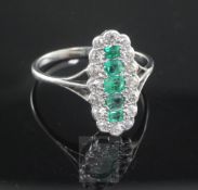 An 18ct white gold and emerald and diamond oval dress ring, the centre set with five graduated