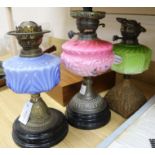 Three Edwardian oil lamps with coloured glass reservoirs