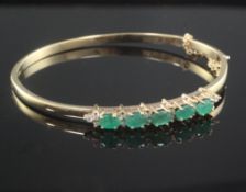 A 9ct gold, emerald and diamond hinged bangle, set with five oval cut emeralds.