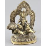 A Tibetan gilt bronze figure of Vaishravana, seated on a lion holding a mongoose on a lotus petalled