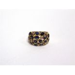 A SAPPHIRE AND DIAMOND BOMBE RING stamped '750', the fifteen randomly set oval cut sapphires with