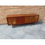 A WILLIAM LAWRENCE 'COSTELLA' TEAK SIDEBOARD fitted with three drawers flanked by cupboards on