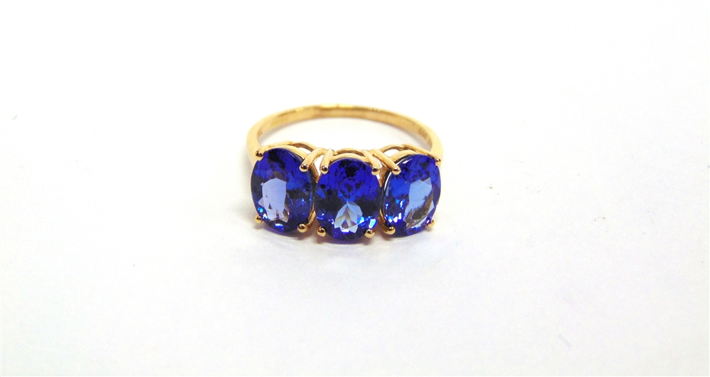 A 14 CARAT GOLD THREE STONE TANZANITE RING set with uniform oval cuts, finger size O 1/2, 2.9g