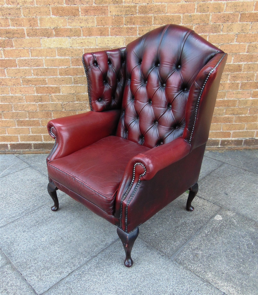 AN UPHOLSTERED RED LEATHER WING ARMCHAIR buttoned and studded and raised on four cabriole