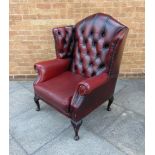 AN UPHOLSTERED RED LEATHER WING ARMCHAIR buttoned and studded and raised on four cabriole