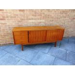 A GORDON RUSSELL TEAK SIDEBOARD fitted with three drawers and sliding doors, 'GORDON RUSSELL LIMITED