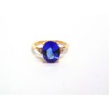 A 14 CARAT GOLD TANZANITE SINGLE STONE RING with a trio of small brilliant cuts to each shoulder,