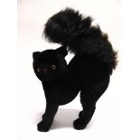 A BLACK MOHAIR PLUSH SOFT TOY CAT with a jointed head and yellow glass eyes, 21cm long.