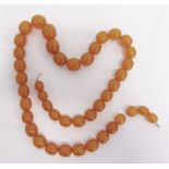A ROW OF AMBER BEADS of graduated ovals, 76cm long, 130g gross