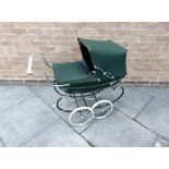 A SILVER CROSS DOLL'S PRAM the lined green metal body with a folding hood and an apron, on a