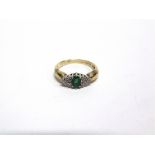 A DIAMOND AND EMERALD 9 CARAT GOLD RING the oval cut stone flanked either side by six single cut