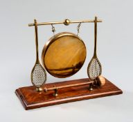 A Victorian novelty tennis dinner gong, the brass gong supported by upright tennis rackets,