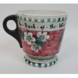 A Mak Merry pottery mug the pink ground hand painted with blossoms and the motto 'The back of the