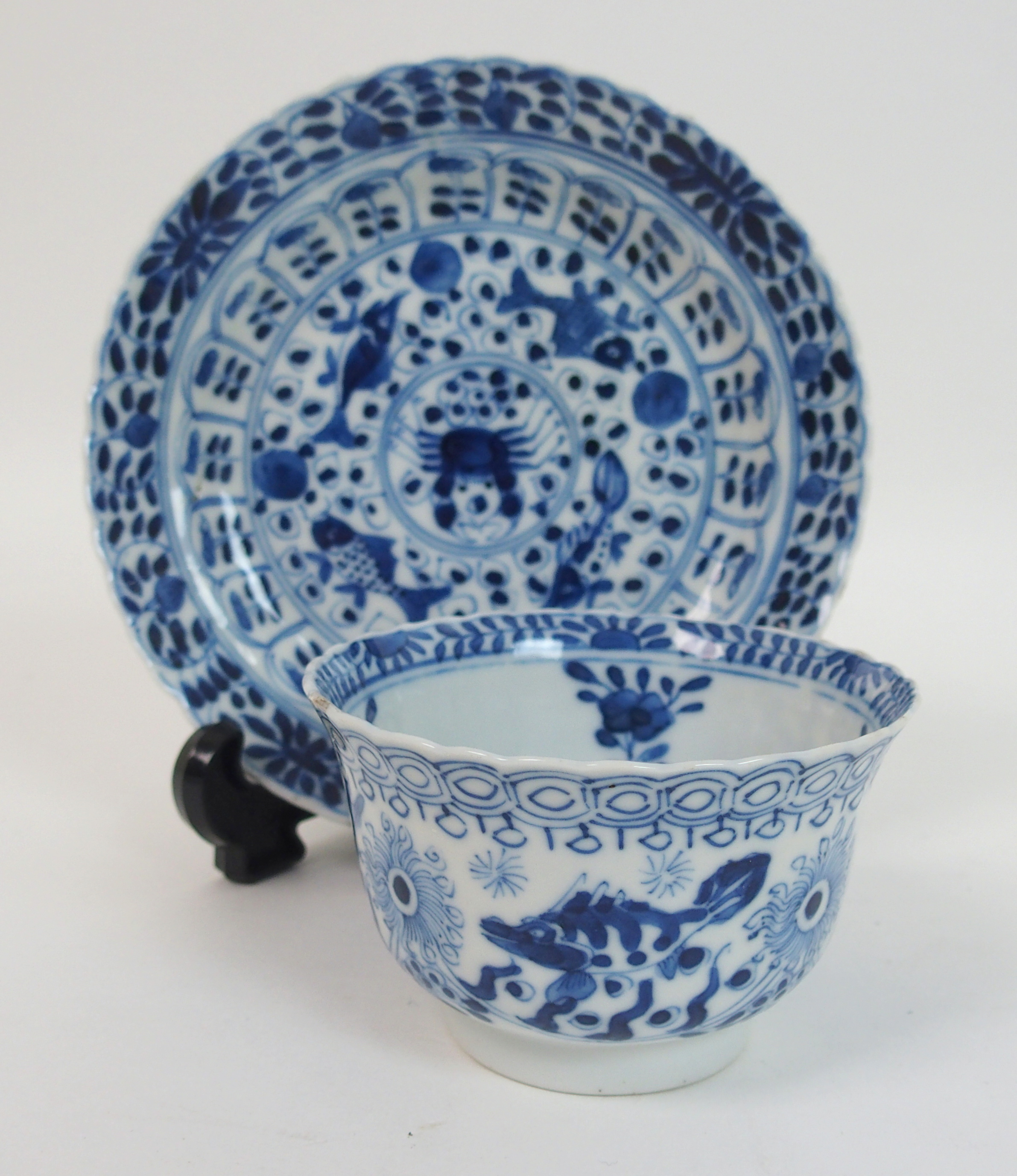 A Chinese blue and white tea bowl and saucer painted with fish surrounding a crab amongst foliage,