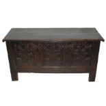 An oak coffer the hinged twin plank top above three carved foliate panels beneath a foliate frieze