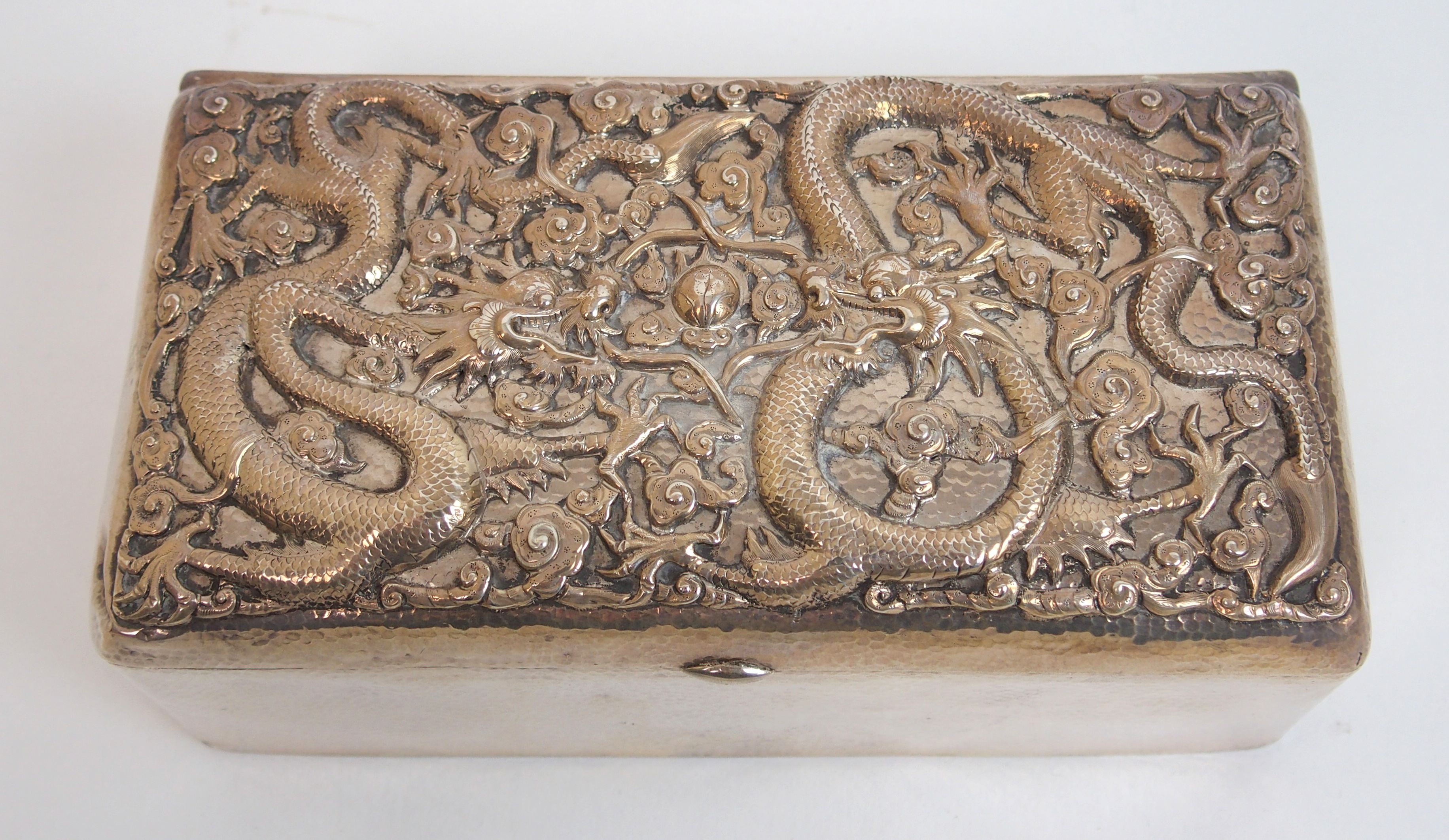 A Chinese silver hammered rectangular cigar box the hinged cover decorated with two facing dragons