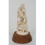 A Japanese ivory okimono of a figure standing and holding a scroll on the back of a grotesque