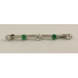 A diamond and emerald bar brooch the central diamond is approx 0.45cts flanked by two emeralds