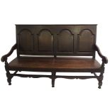 A 19th Century oak four seat hall bench with arched panel back joined by scroll arms, solid seat and