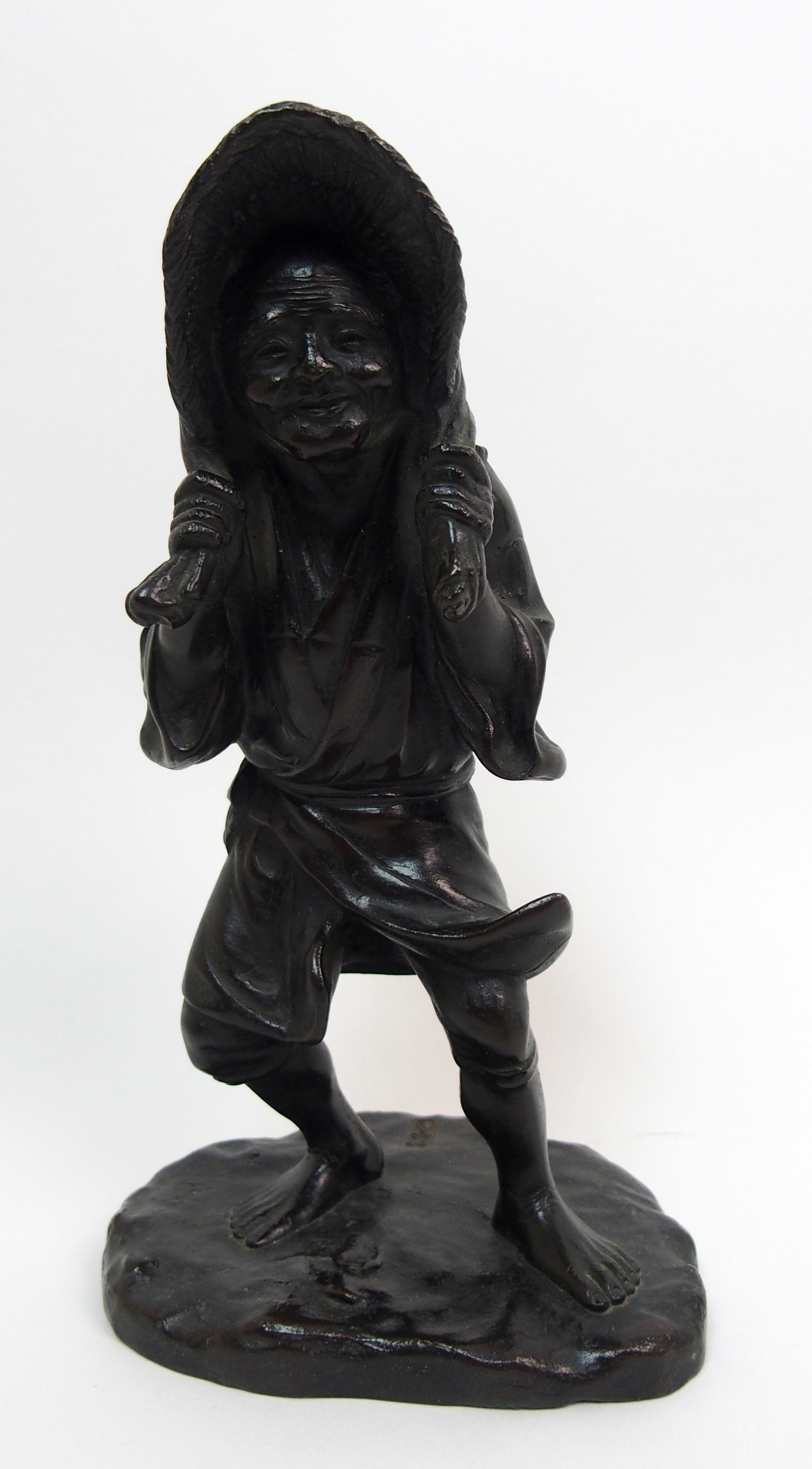 A Japanese bronze figure of a worker standing and holding straw hat around her head and on a mound