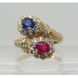 A bright yellow metal dress ring set with diamonds a ruby and a sapphire of twin cross over flower