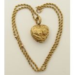 A bright yellow metal heart shaped locket with raised design on the front of a stately home,