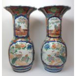 A pair of Arita large baluster vases painted with panels of peacocks beside rivers and amongst