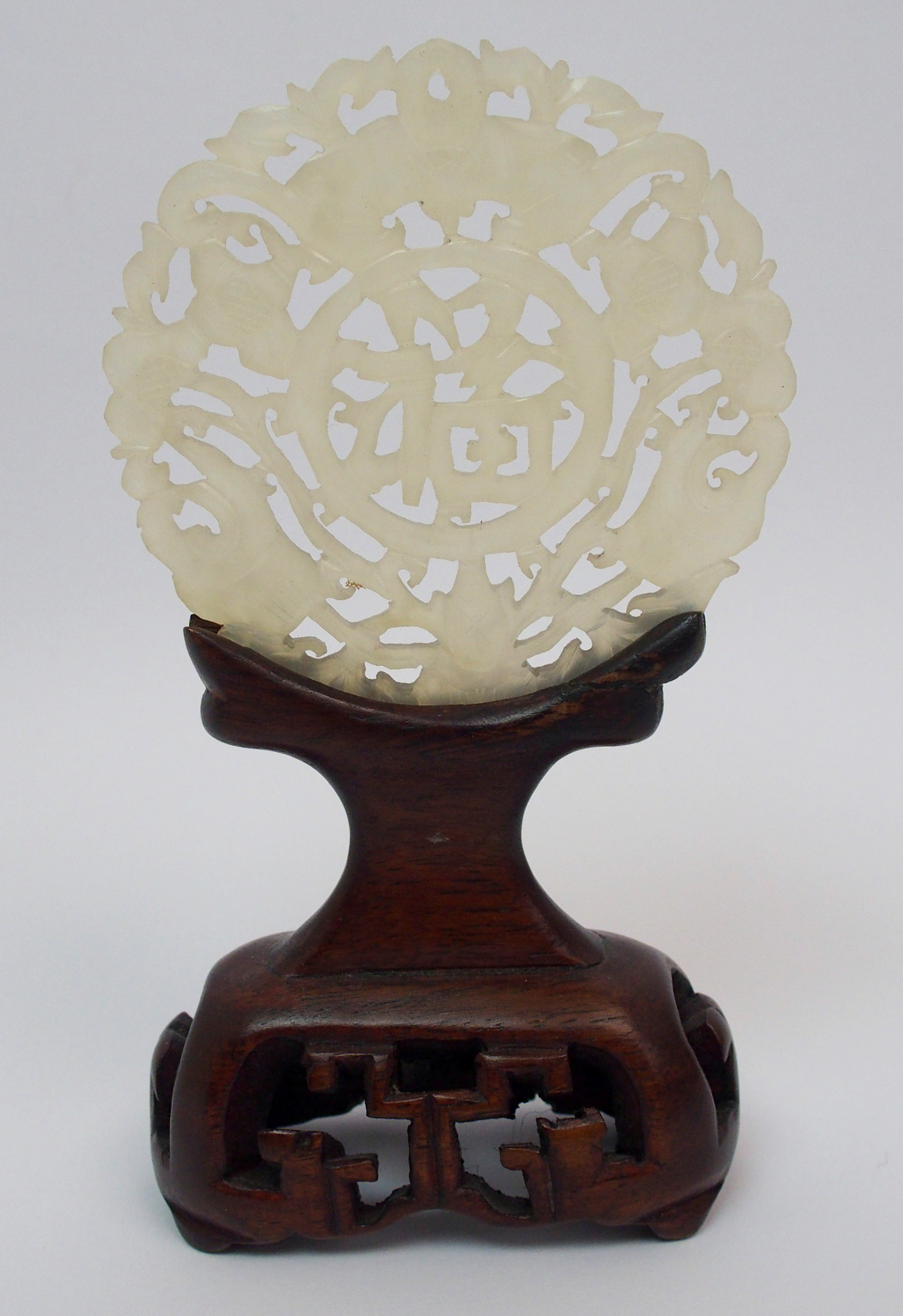 A Chinese hardstone medallion carved with bats surrounding characters, 7cm diameter, wood stand