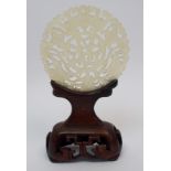 A Chinese hardstone medallion carved with bats surrounding characters, 7cm diameter, wood stand