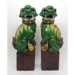 A pair of Chinese famille verte buddhistic lions standing on square bases and resting on a cub and