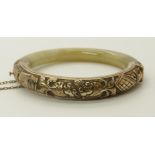 A Chinese green hardstone bangle with a gilded white metal panel embossed with fancy gold fish,