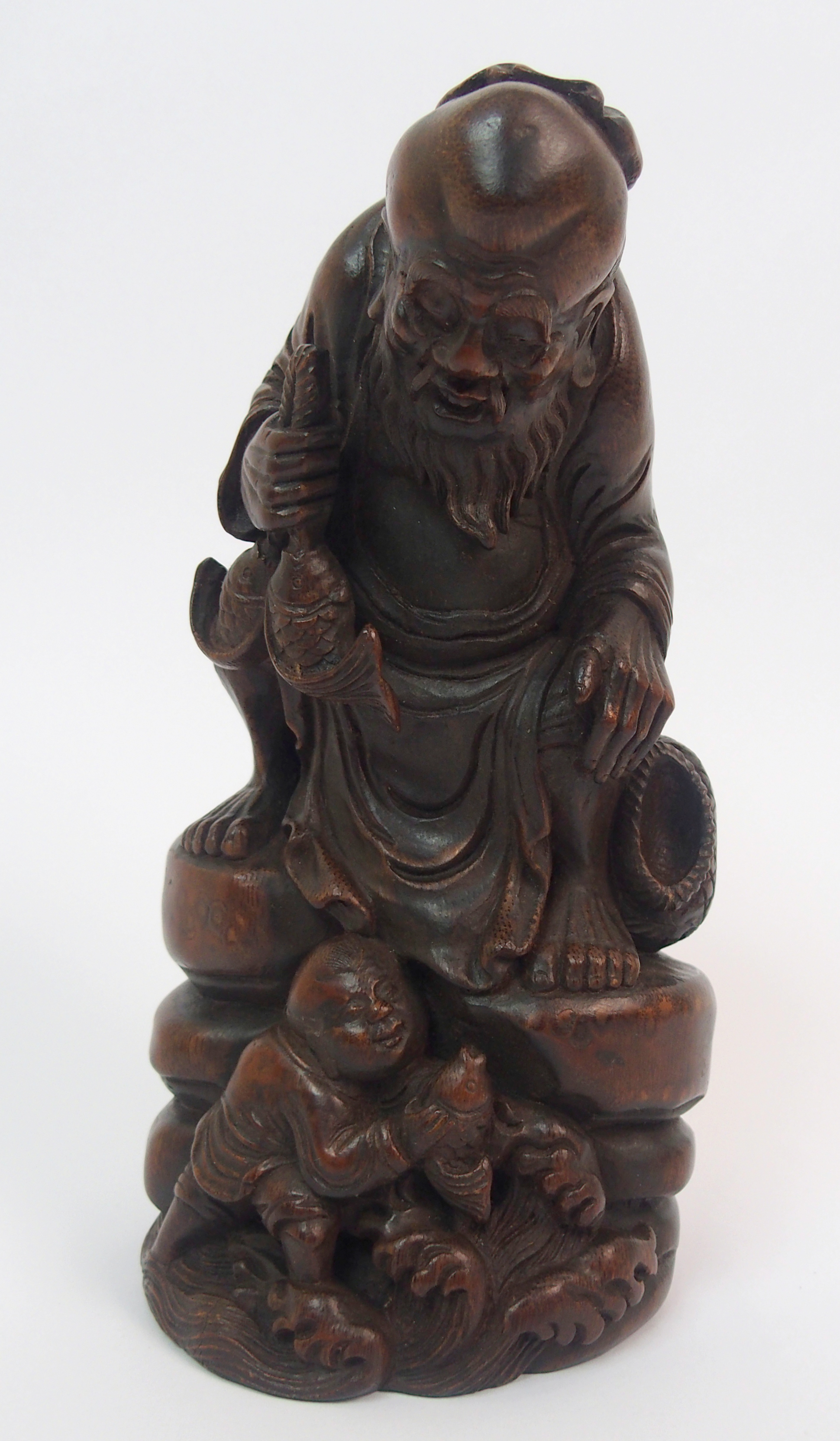 A Chinese bamboo figure of a fisherman seated on a rock above a young boy holding a fish amongst