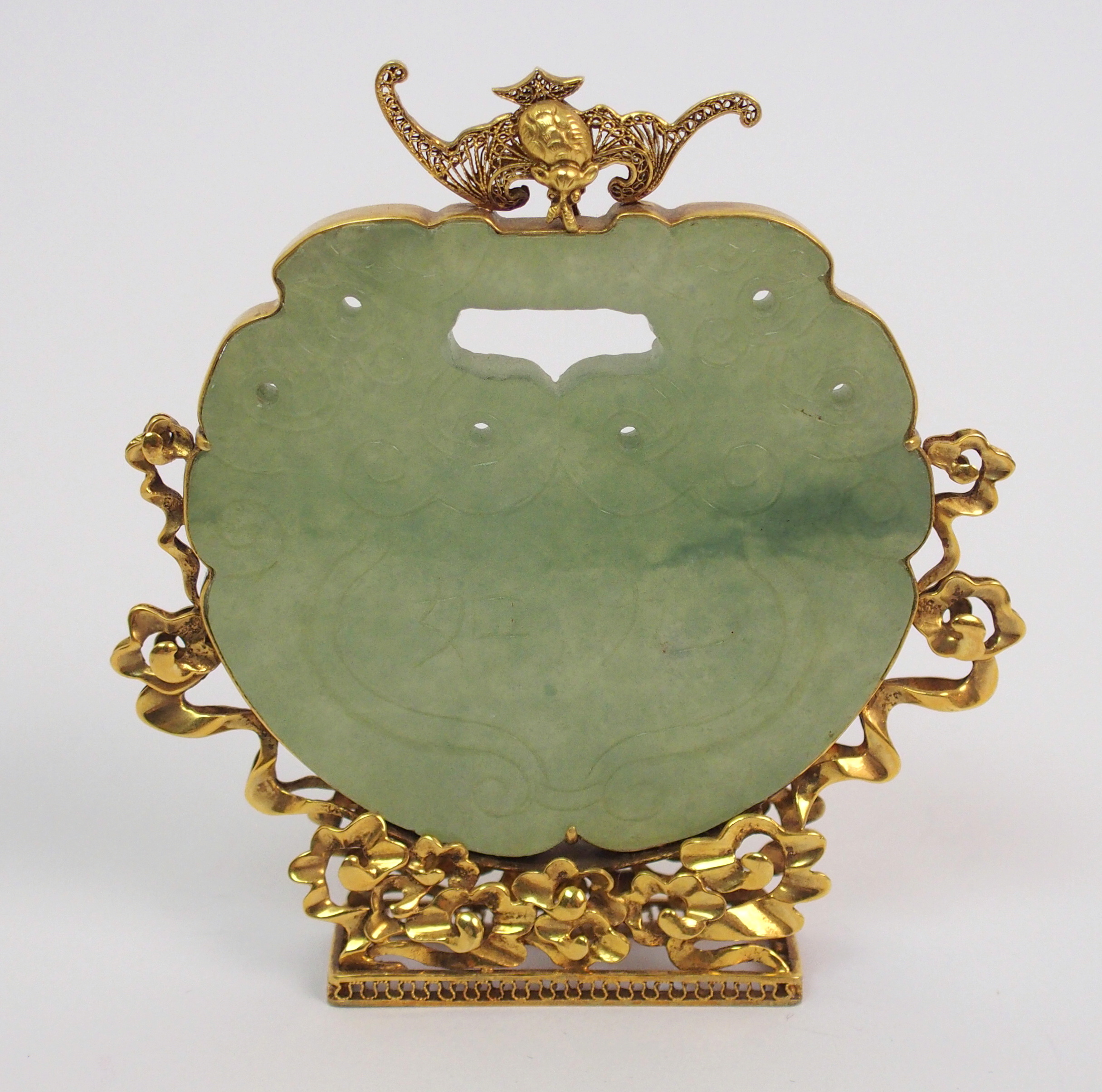 A Chinese hardstone pendant disc carving with conjoined grotesques, set within a gilt metal