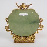 A Chinese hardstone pendant disc carving with conjoined grotesques, set within a gilt metal