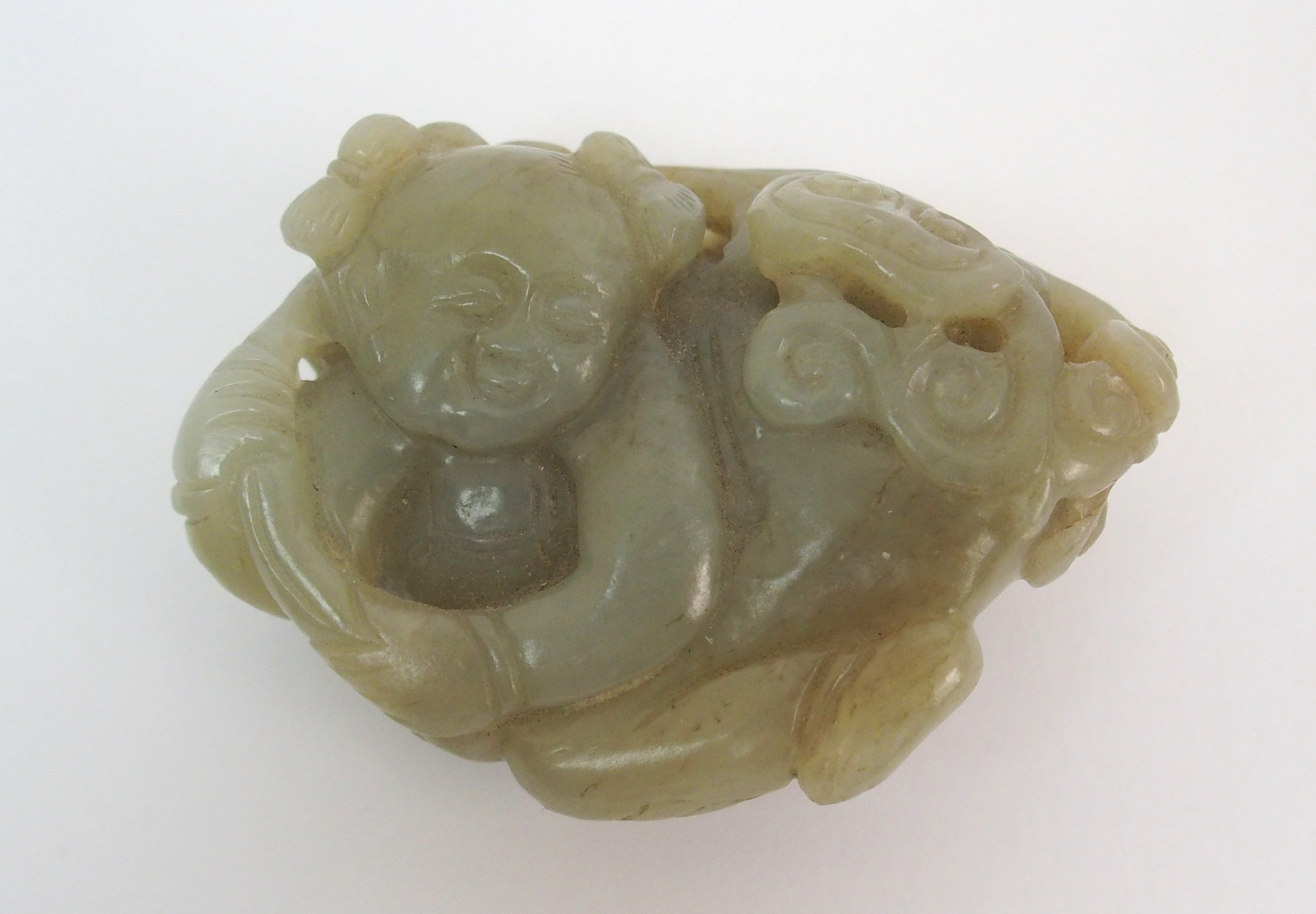 A Chinese jade carving of a child lying and holding lingzhi frond, 7cm wide