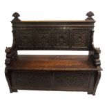 A Victorian oak hall settle with fruit finials above geometric panels above a hinged seat with