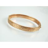 A 9ct rose gold hollow hinged bangle, with bright cut engraved scroll and foliate decoration,