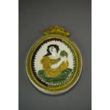 An early 19th century oval Prattware plaque decorated in relief with a brunette maiden holding a