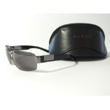 A pair of Gucci sunglasses, dark metal frame and Gucci logo to temple